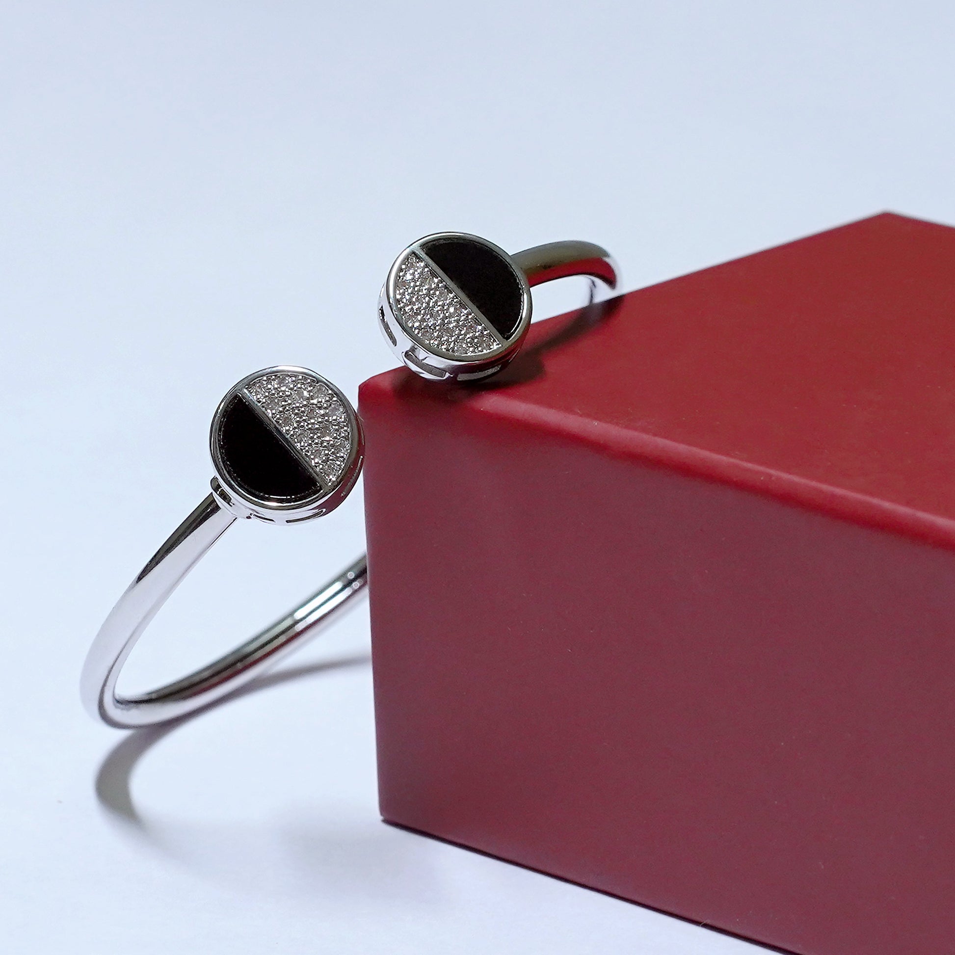 Silver bracelet with black stones on a red box against a light blue background