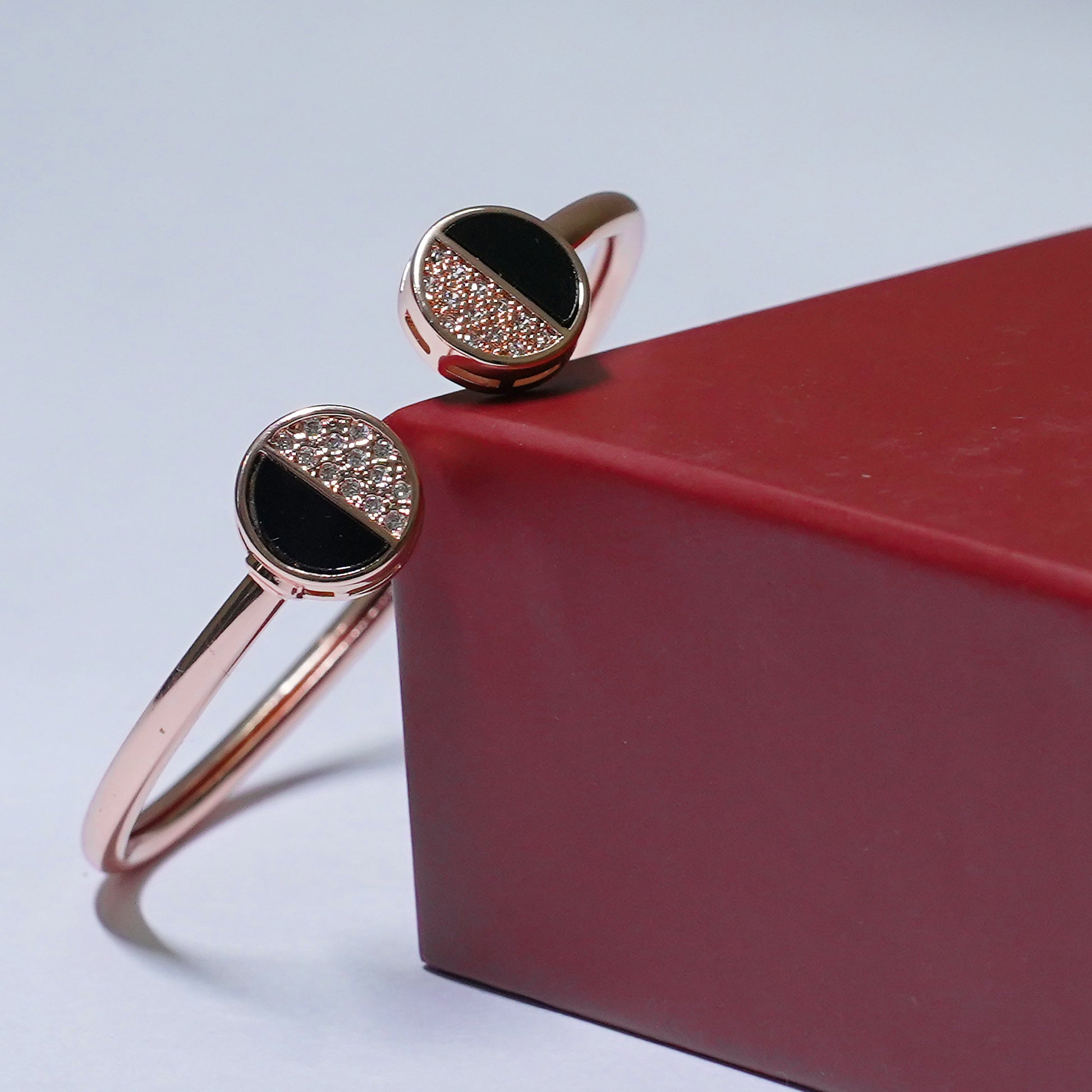 Rose gold bracelet with black gemstones on a red box against a light gray background