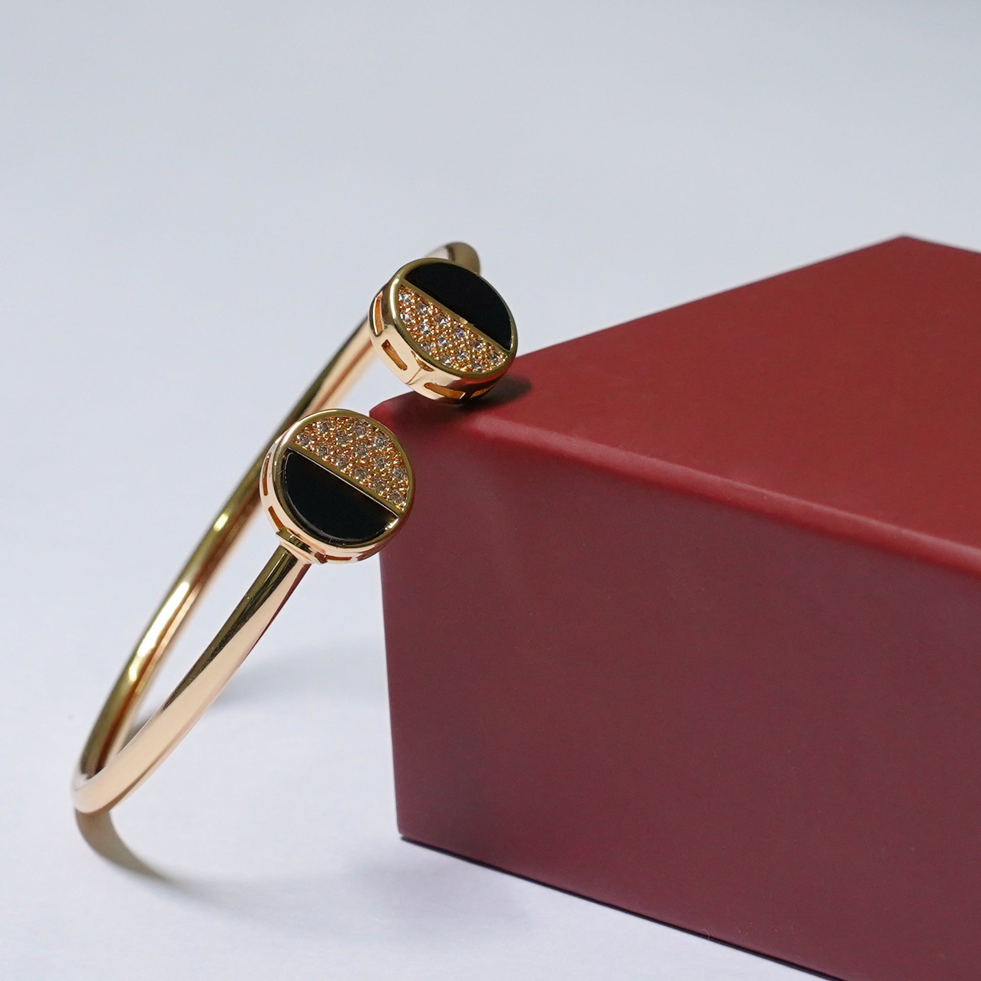 Gold bracelet with black stones on a red box against a light gray background